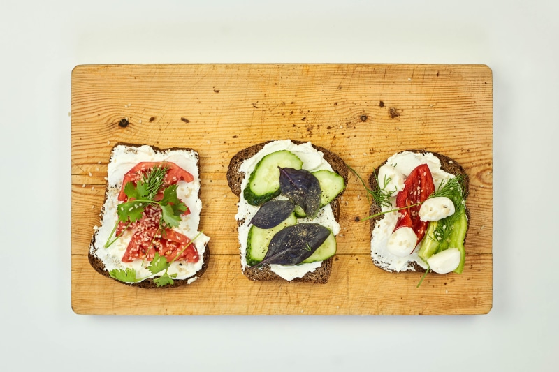 Three open-faced sandwiches with vegetables on a cutting board