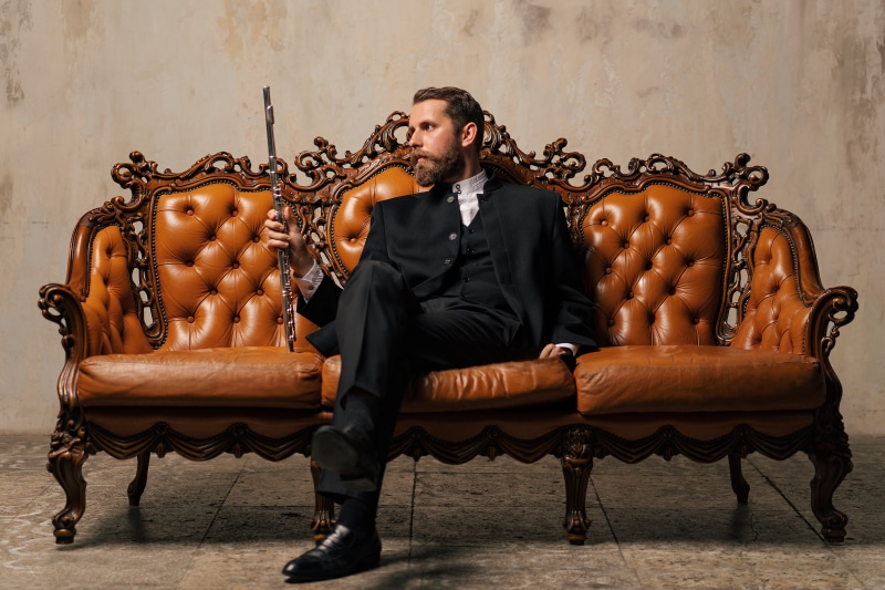 Yaroslav Kotov in a suit with a flute on a sofa