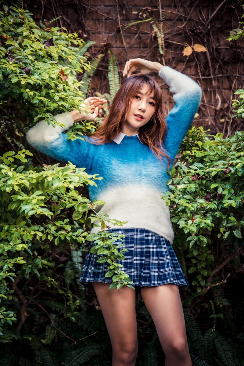 Asian woman in sweater and skirt posing in foliage