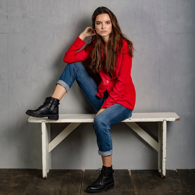 Woman in red suit jacket and jeans sitting on bench