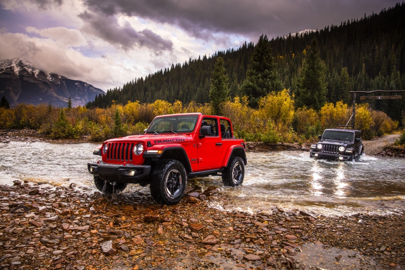 Red and black Jeep Wranglers crossing a river