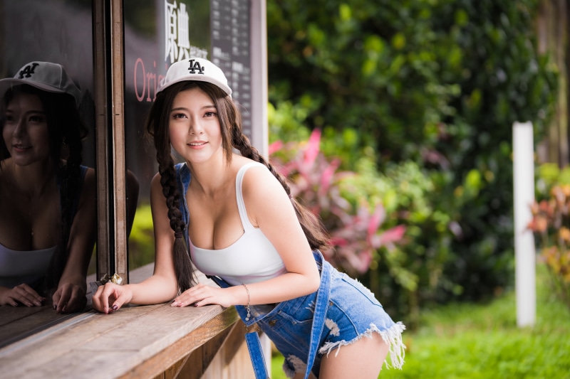 Asian woman with braids wearing a baseball cap and denim overalls