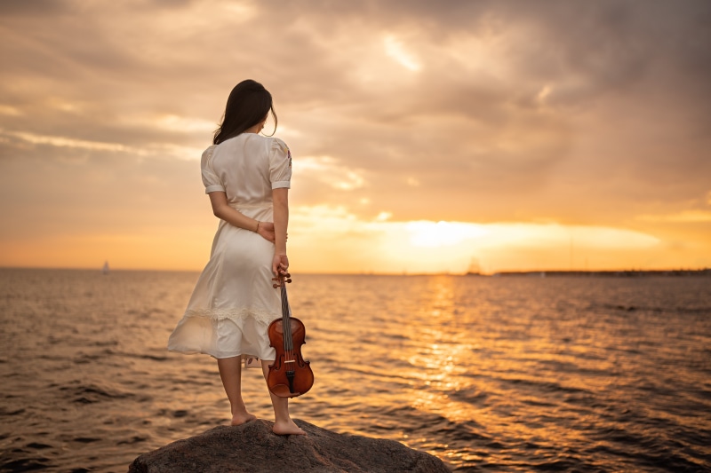 Woman with violin by the sea at sunset