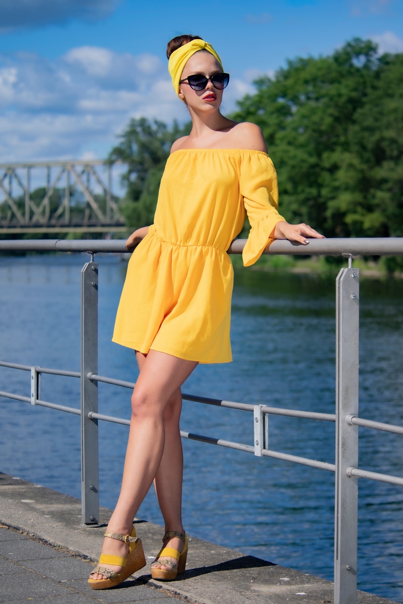 Woman in yellow dress and sunglasses posing by railing
