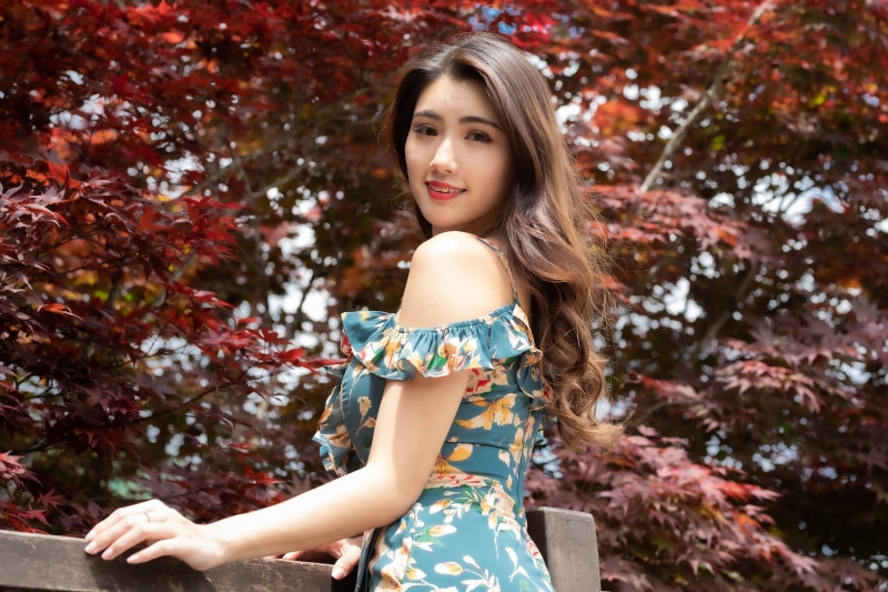 Asian woman in floral dress posing near red leaves