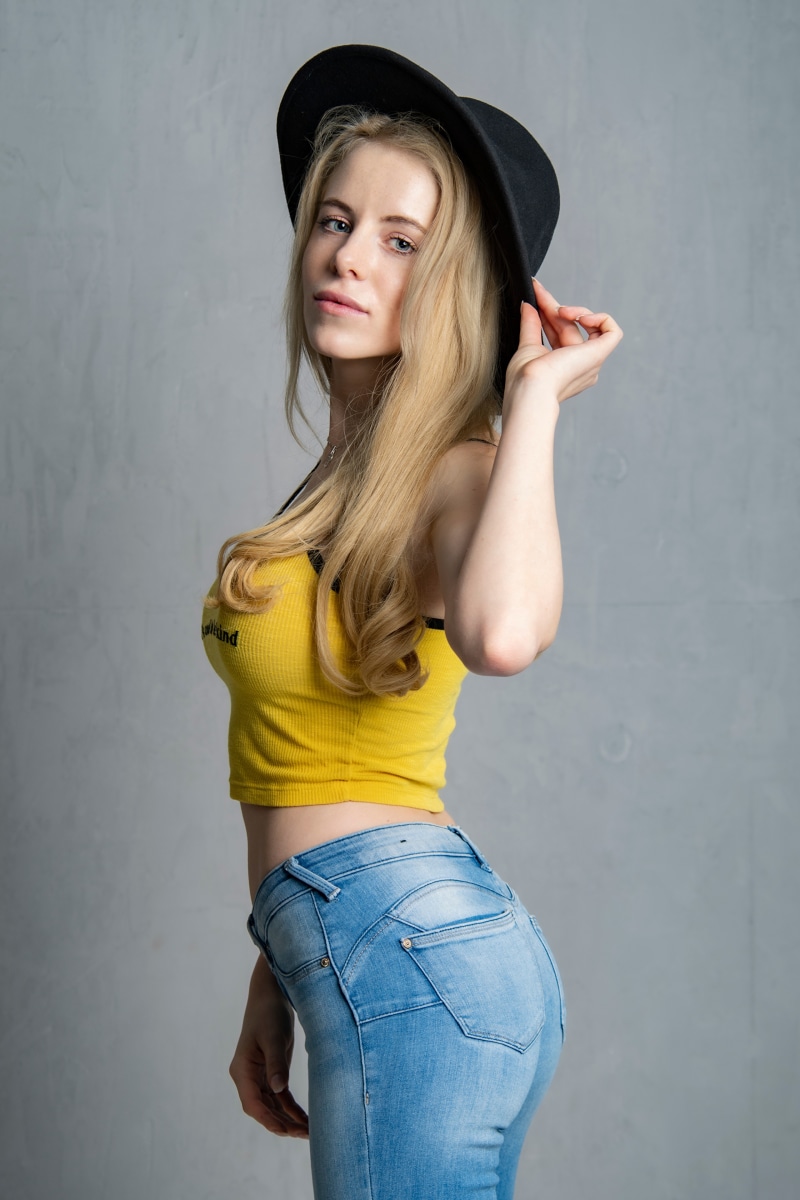 Blonde girl wearing a hat, jeans, and a yellow singlet
