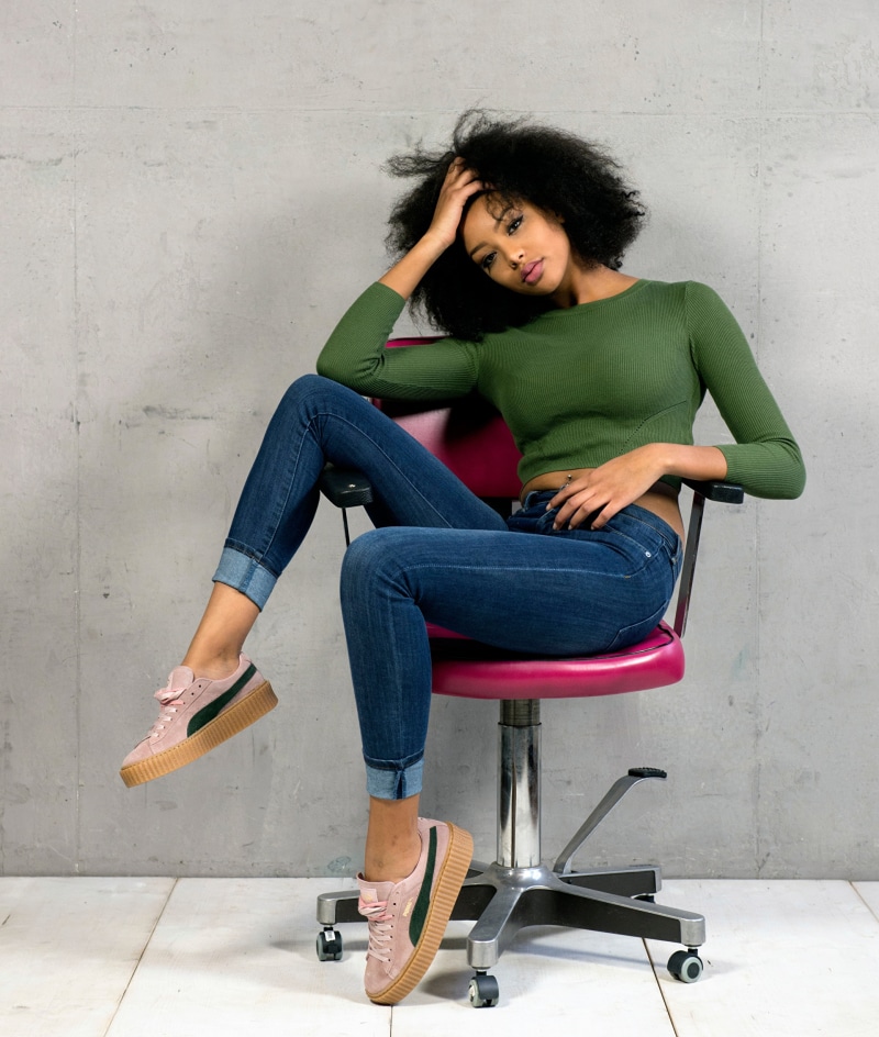 Sainabou sitting on a chair wearing jeans and Puma sneakers