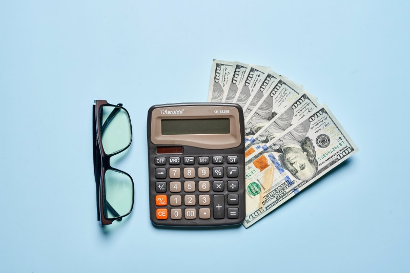 Calculator, Glasses, and US Dollar Bills on Blue Background