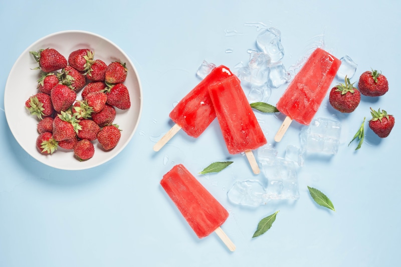Strawberries and popsicles with ice on a blue background
