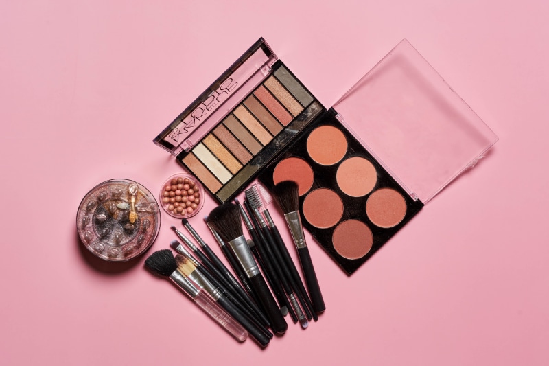 Makeup brushes and palettes on pink background