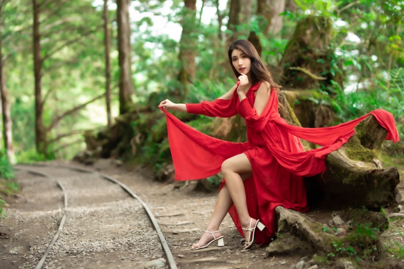 Woman in red dress sitting by train tracks in forest