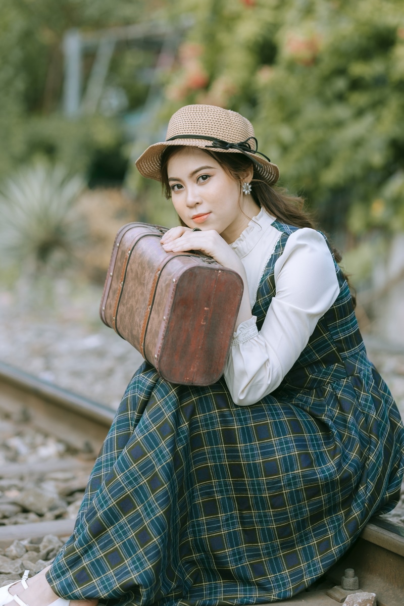 Woman in vintage dress and hat with suitcase on train tracks