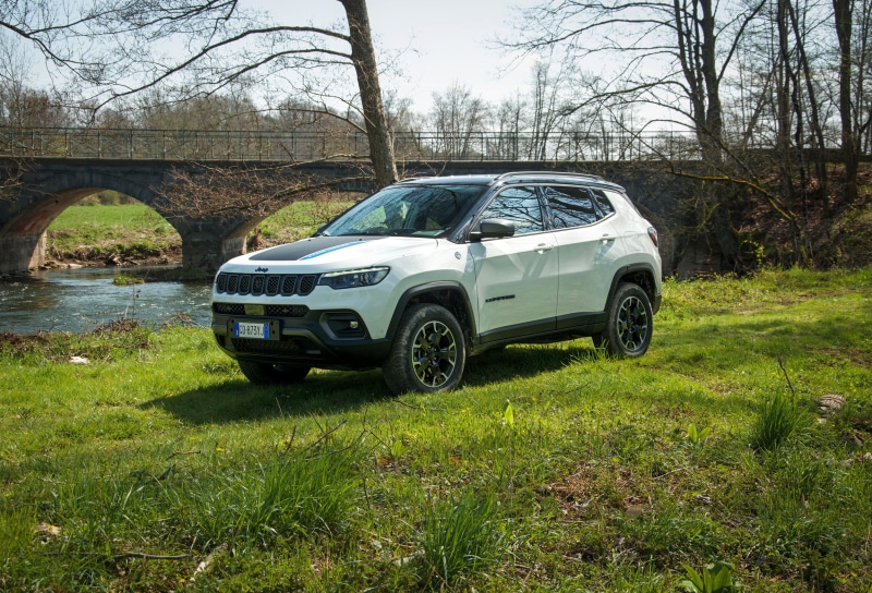 White Jeep Compass Trailhawk 4xe parked by a river and bridge