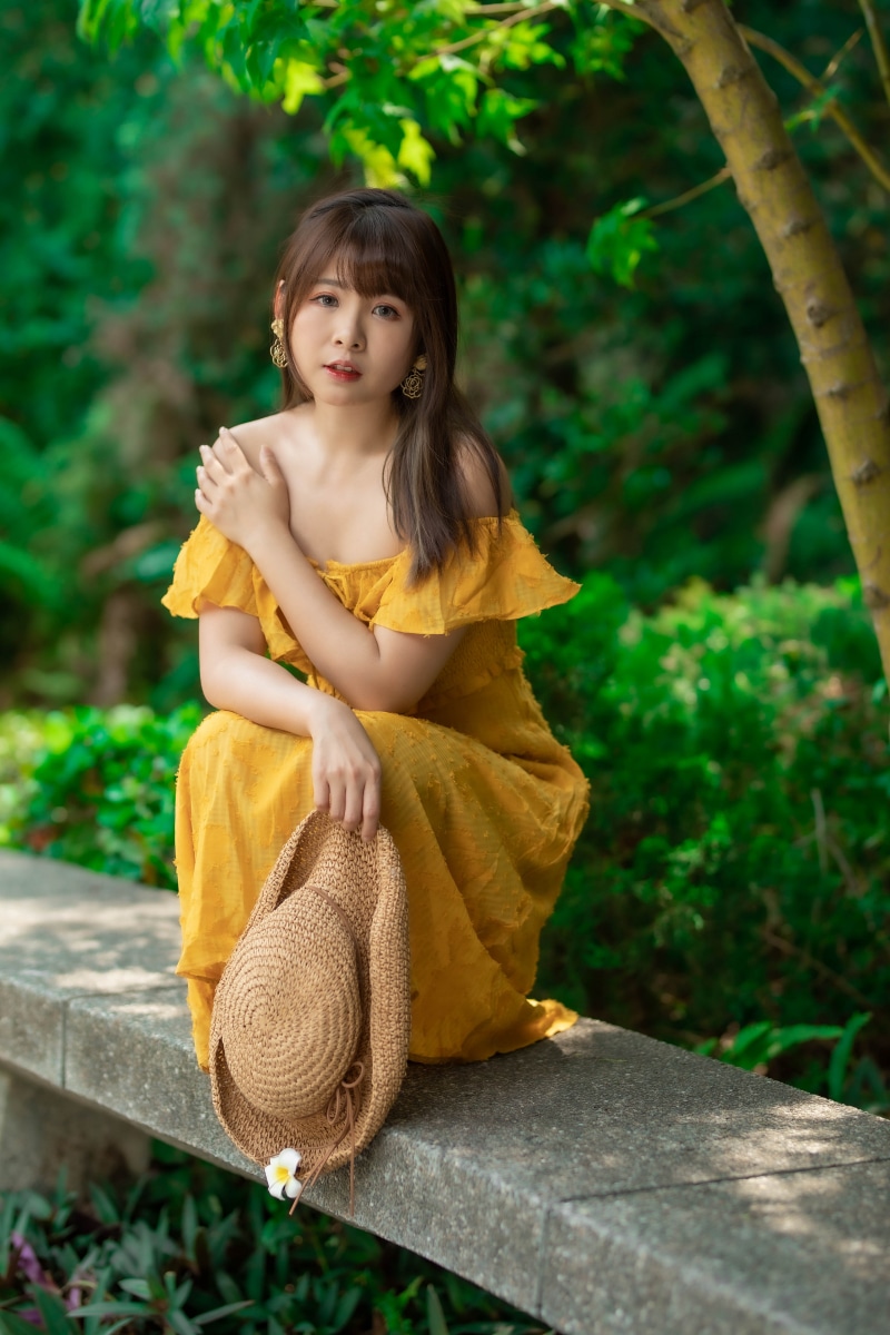 Asian woman in yellow dress holding a hat