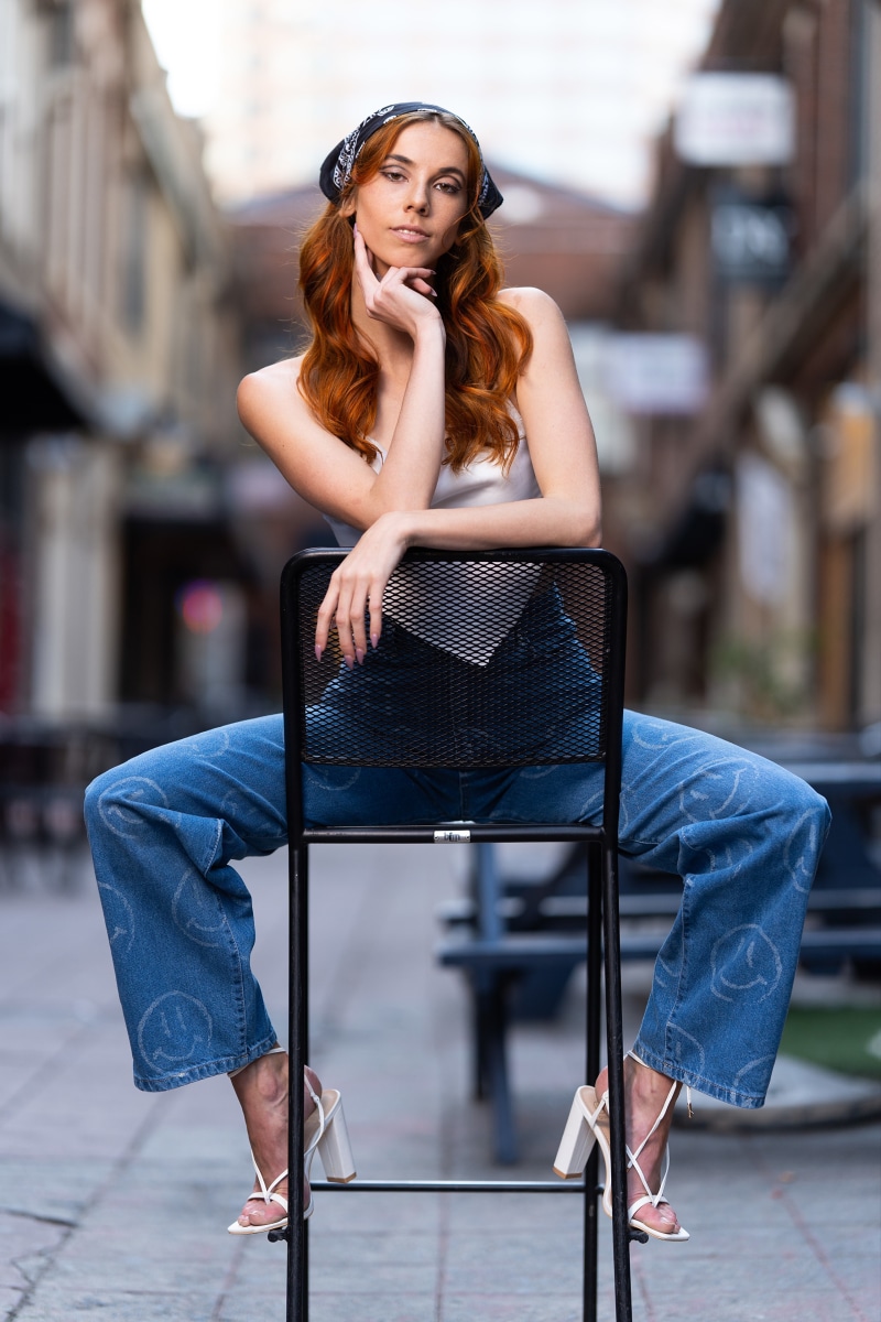 Woman with red hair wearing bandana and jeans sitting on chair