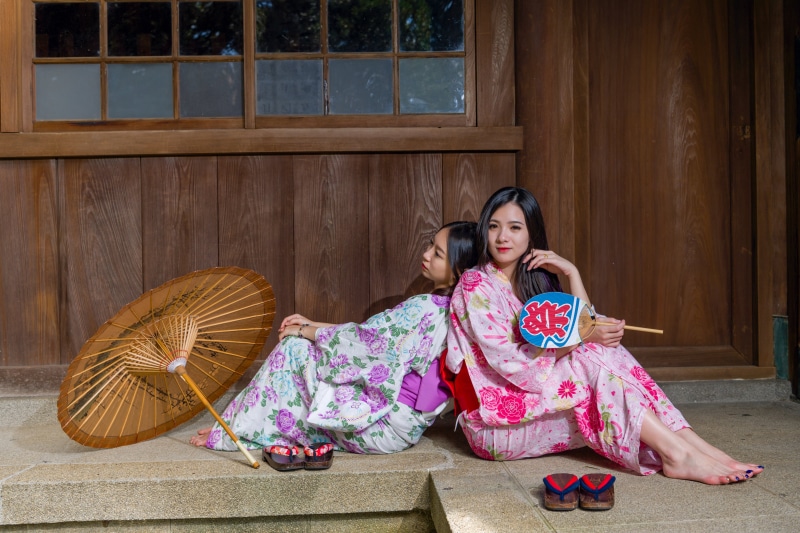 Two Asian women in kimonos with umbrellas and fans