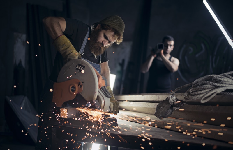 Man using a circular saw with sparks flying, another man filming