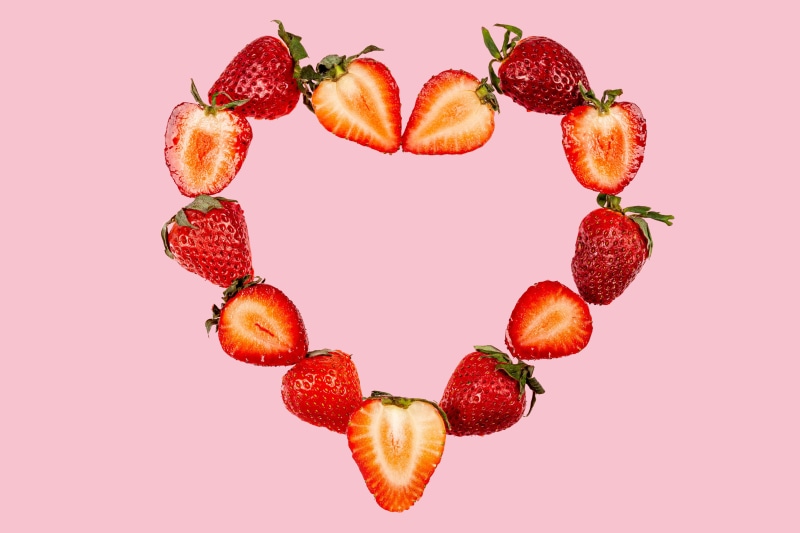 Strawberries arranged in a heart shape on a pink background