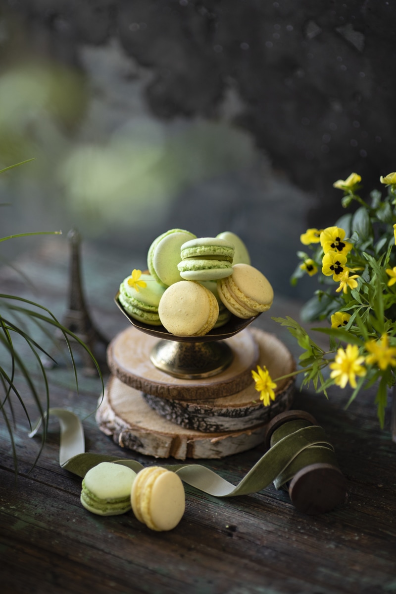 Green and yellow macarons on a wooden table with flowers