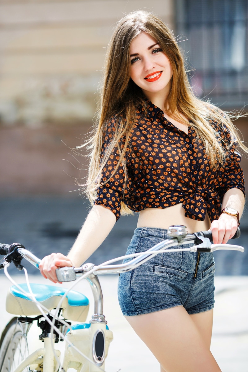 Woman with brown hair and red lips posing with a bicycle