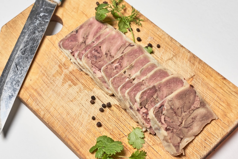 Sliced meat terrine on a cutting board with knife