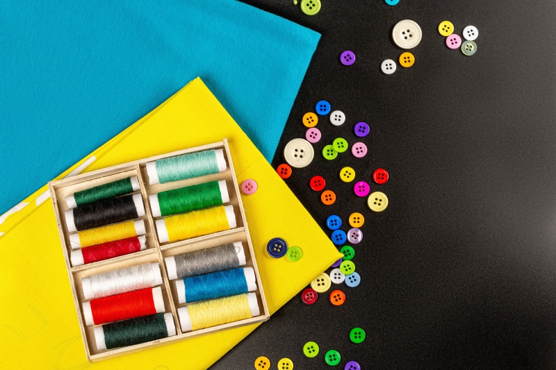 Sewing supplies with threads and buttons on gray background