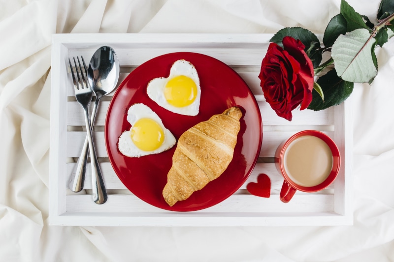 Breakfast tray with heart-shaped eggs, croissant, coffee, and rose