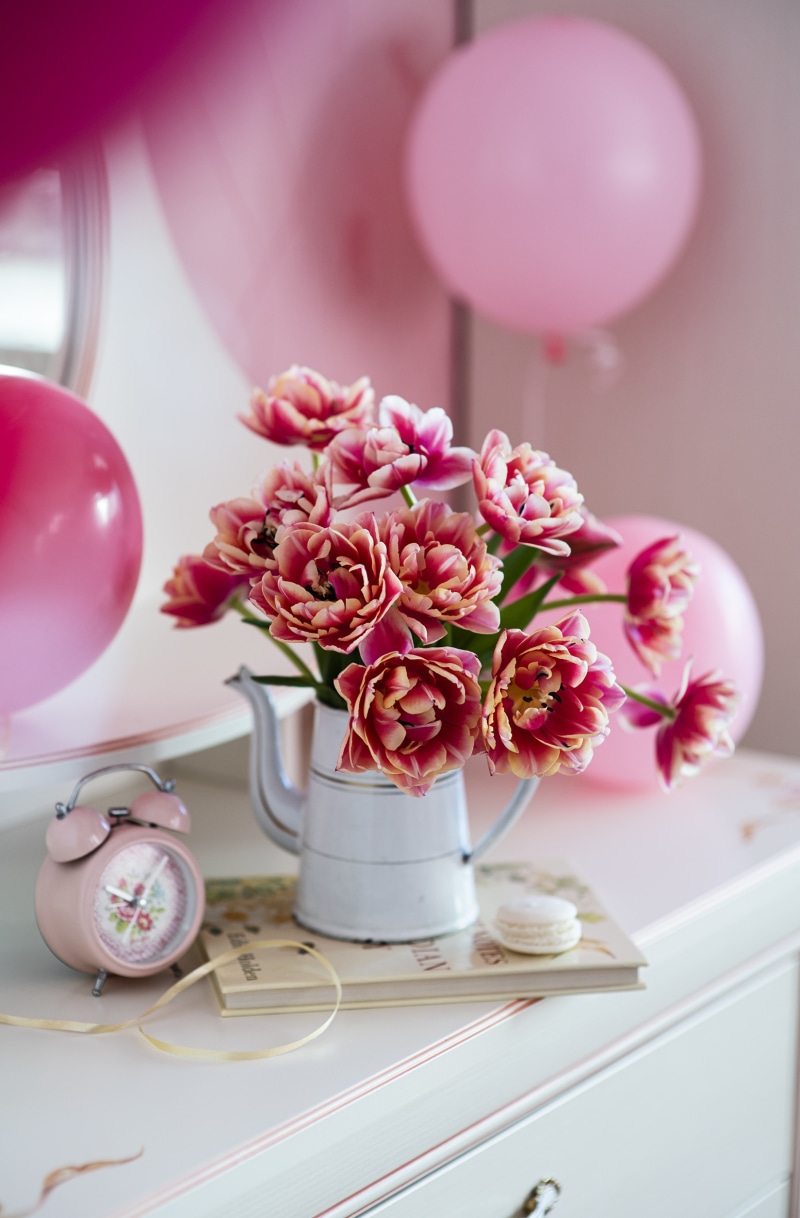 Pink tulips in a vase with balloons and an alarm clock