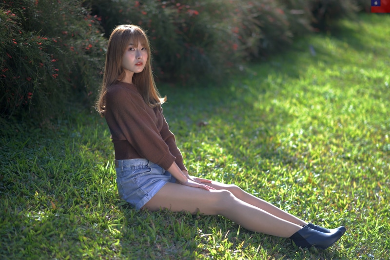 Asian woman sitting on grass wearing shorts and sweater
