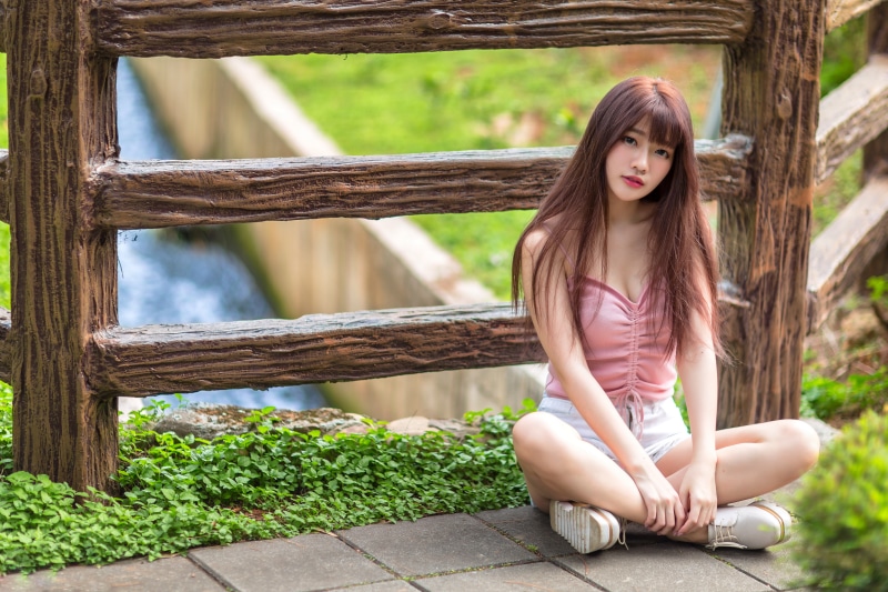 Asian woman sitting by a wooden fence