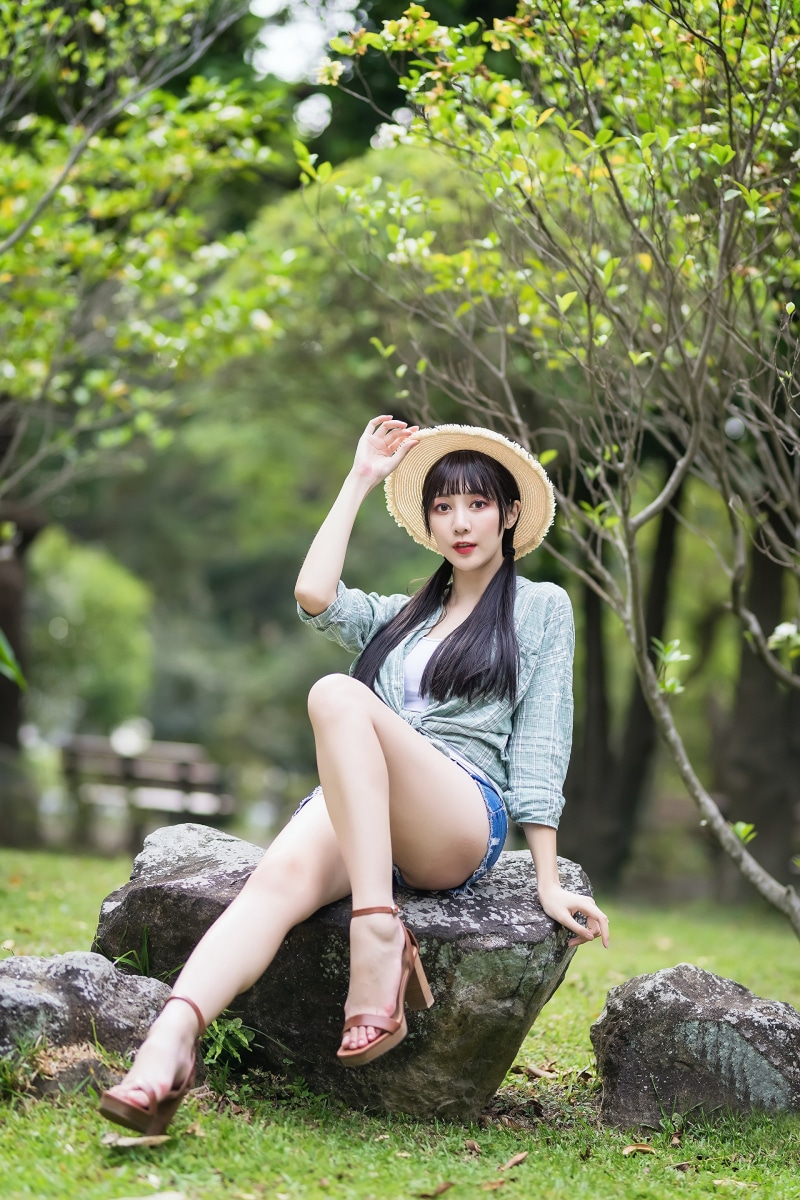 Asian woman with hat sitting on rocks in park