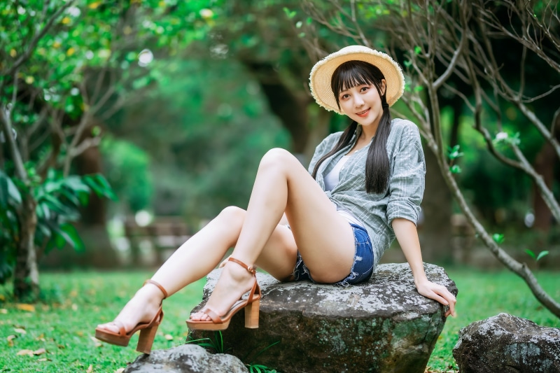Asian woman in straw hat and shorts sitting on rocks
