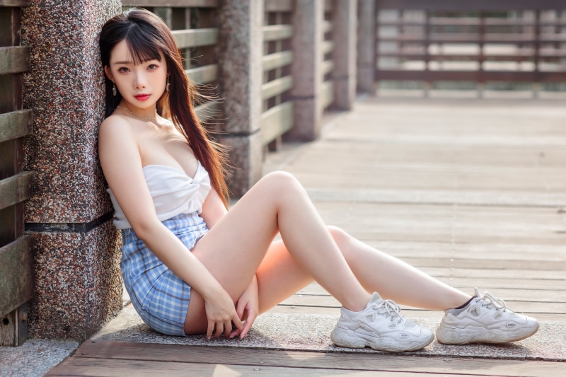 Asian woman in skirt and sneakers sitting on a boardwalk