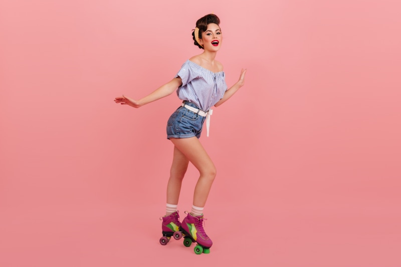 Woman with roller skates and shorts on pink background