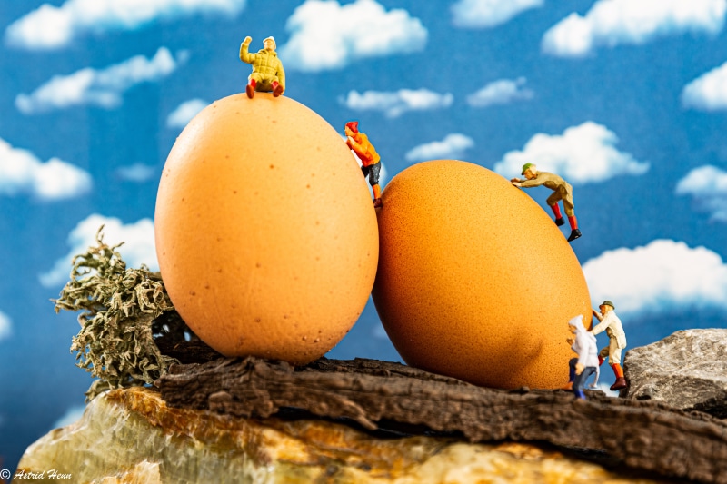 Miniature figures climbing eggs against a cloudy sky