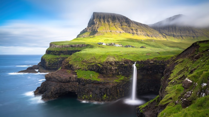 Waterfall cascading off a cliff into the sea near a village
