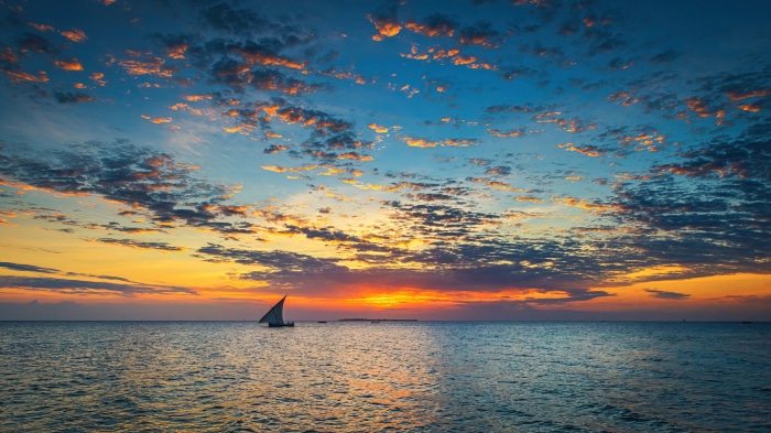 Sailboat on the ocean at sunset with clouds
