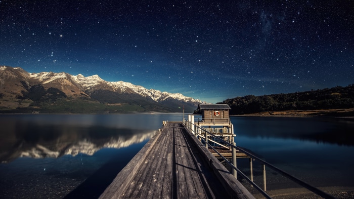 Wooden pier under starry sky with snow-capped mountains