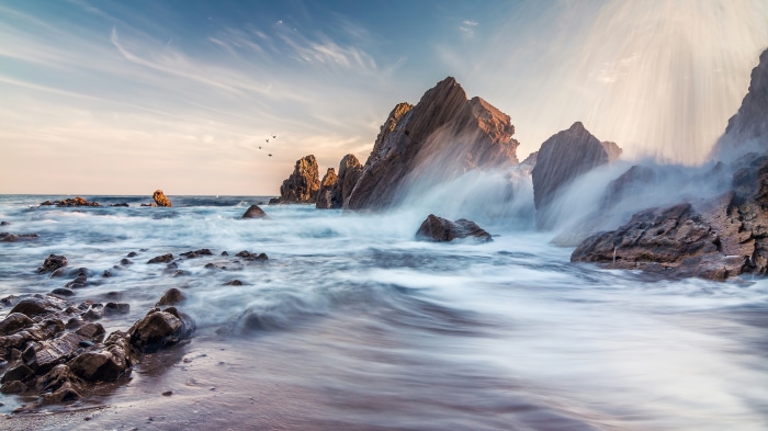 Waves crashing on rocky shore with birds in the sky