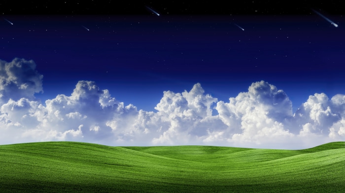 Night sky with shooting stars over rolling green hills and clouds