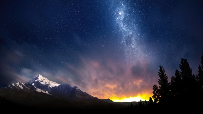 Starry night sky over snow-capped mountains and forest