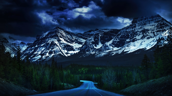 Dark Mountain Road Through Forest with Snow-Capped Peaks
