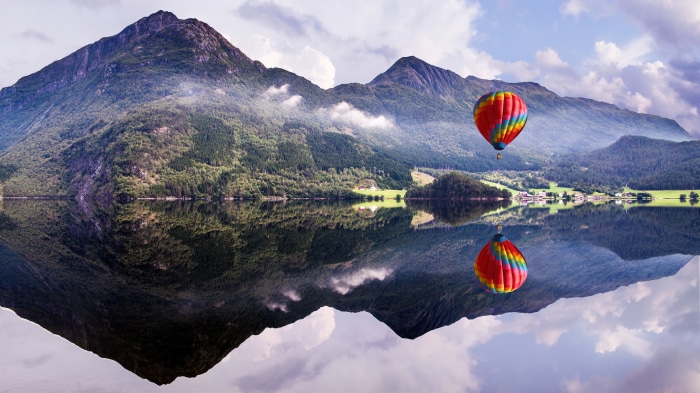 Hot air balloon over a lake with mountains and reflection 4K