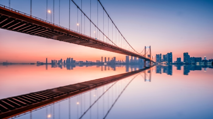 Suspension bridge over a river with city skyline at sunset 4K