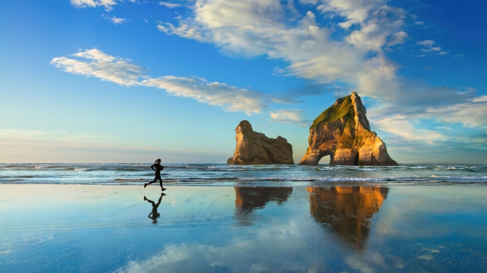 Woman jogging on beach with rock formations, 4K