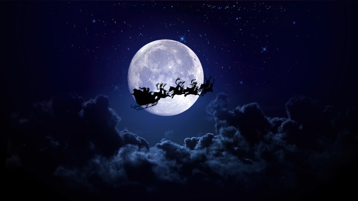 Santa Claus flying with reindeer and sleigh in front of moon 4K