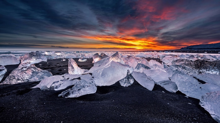 Icebergs on black sand beach during sunset