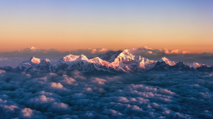Sunrise over snow-capped mountains above clouds in 4K