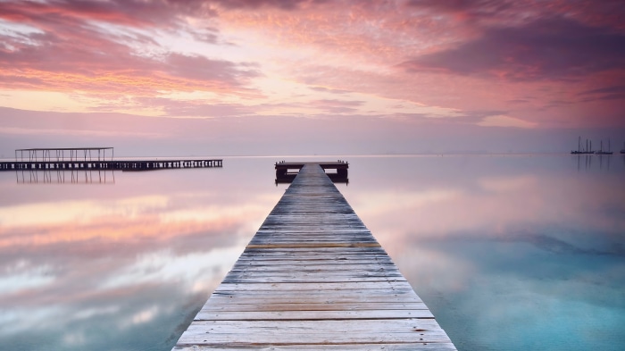 Wooden pier on calm sea at sunrise with pink clouds