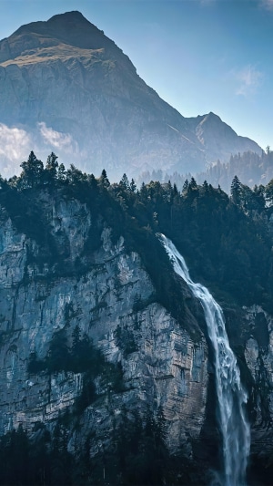 Waterfall cascading down a rocky mountain face with a peak in the background